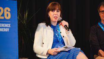 Seated woman in blue dress and white jacket speaking into microphone at panel